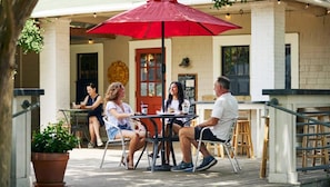 An outdoor patio with a table and chairs under a red umbrella, a brick wall, and a chalkboard sign.