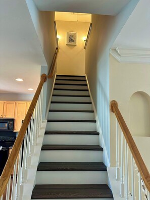 A staircase with wooden handrails, white walls, and a framed picture at the top.