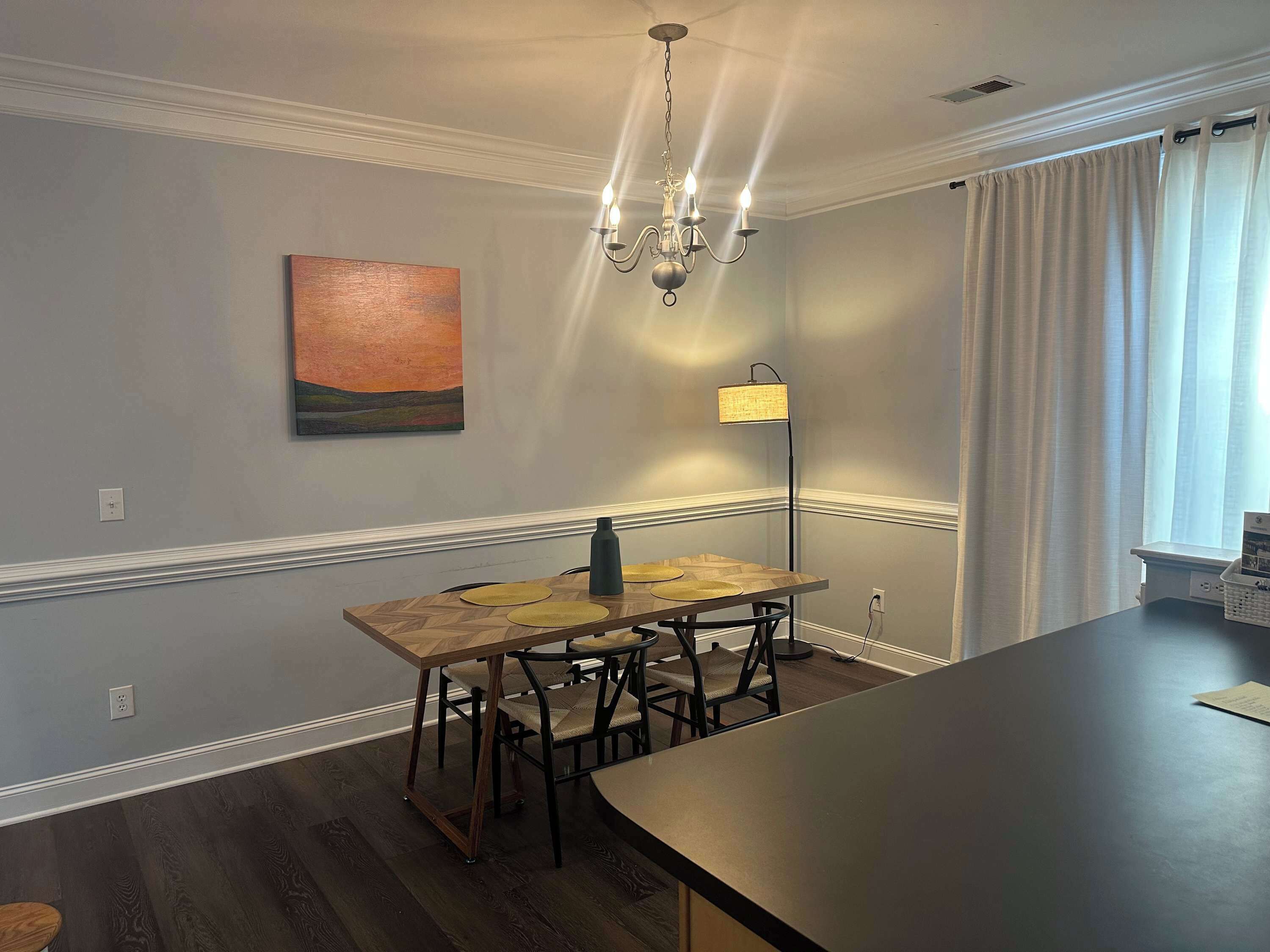 A dining area with a wooden table and chairs, a chandelier, a floor lamp, and a painting on the wall.