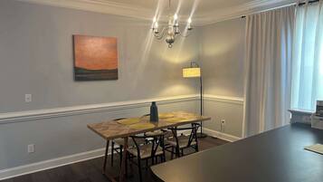 A dining area with a wooden table and chairs, a chandelier, a floor lamp, and a painting on the wall.