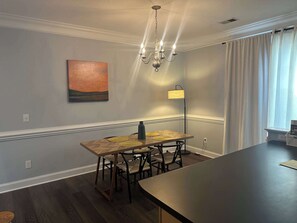 A dining area with a wooden table and chairs, a chandelier, a floor lamp, and a painting on the wall. - 21-322 Pine Street - Cozy Corner Oasis (Cornelius)