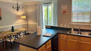 Ett modernt kök med en central köksö, träskåp, en inbyggd diskmaskin och ett fönster med persienner.