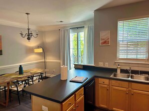 A modern kitchen with a central island, wooden cabinets, a built-in dishwasher, and a window with blinds.