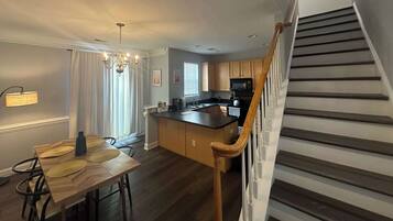 A modern kitchen with a wooden island, a dining area with a table and chairs, and a staircase with wooden railings.