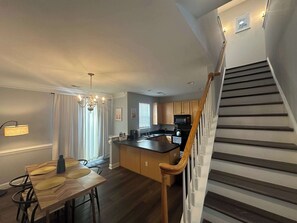 A modern kitchen with a wooden island, a dining area with a table and chairs, and a staircase with wooden railings. - 21-322 Pine Street - Cozy Corner Oasis (Cornelius)