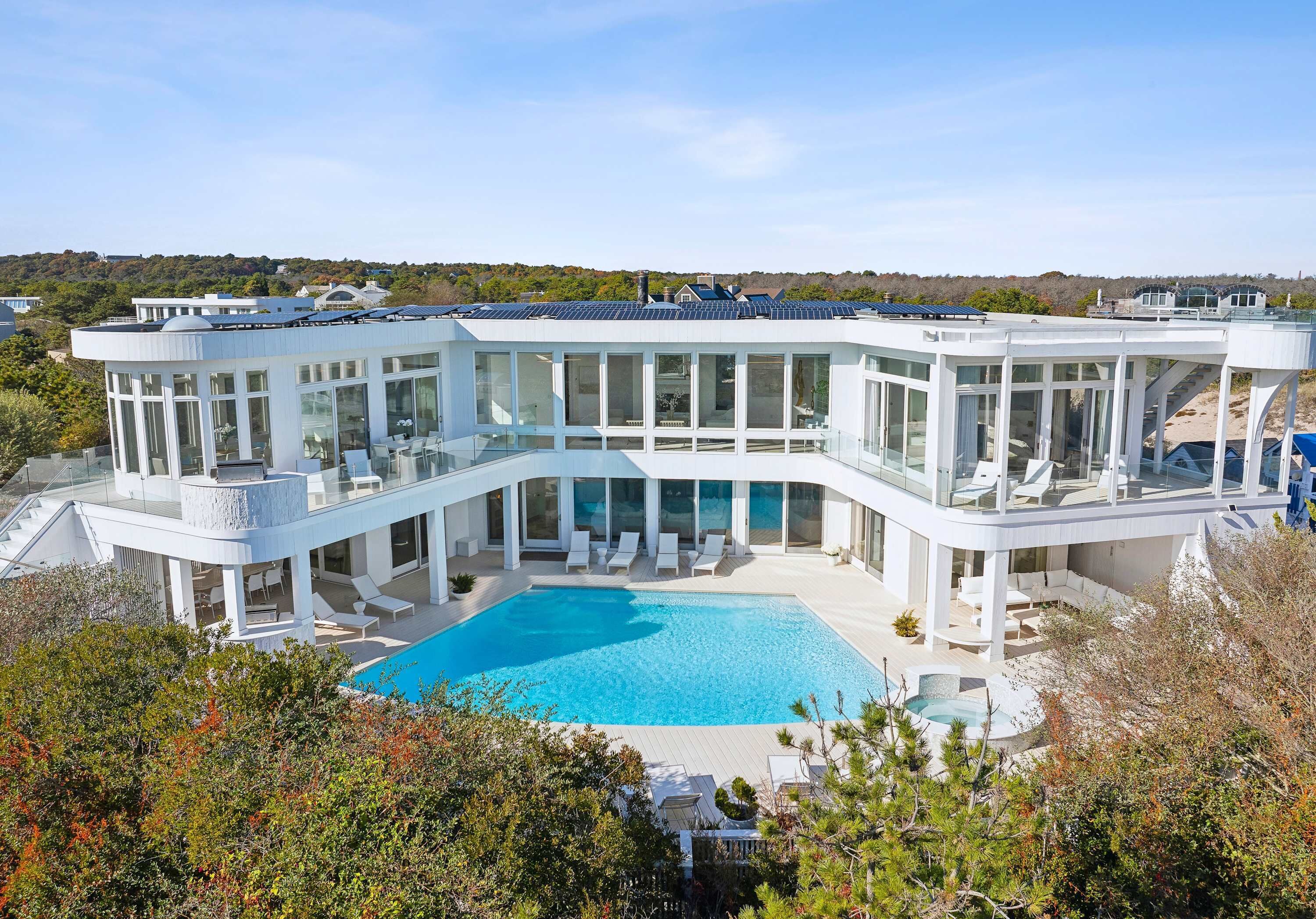 Uma casa moderna com uma piscina grande, varandas envidraçadas e vista para a paisagem circundante.