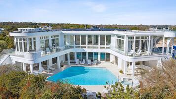 Uma casa moderna com uma piscina grande, varandas envidraçadas e vista para a paisagem circundante.