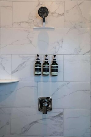 A bathroom with marble tiles, a showerhead, and three bottles of shampoo. - Downtown Urban Retreat 6 Beds Perfect for Groups (Roanoke)