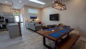 A modern kitchen with a central island, a dining area with a wooden table and benches, a living area with sofas, and a flat-screen TV mounted on the wall. - Downtown Urban Retreat 6 Beds Perfect for Groups (Roanoke)