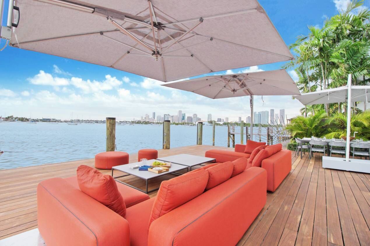 A wooden deck with orange seating, a table with a fruit bowl, and a view of the water and city skyline.