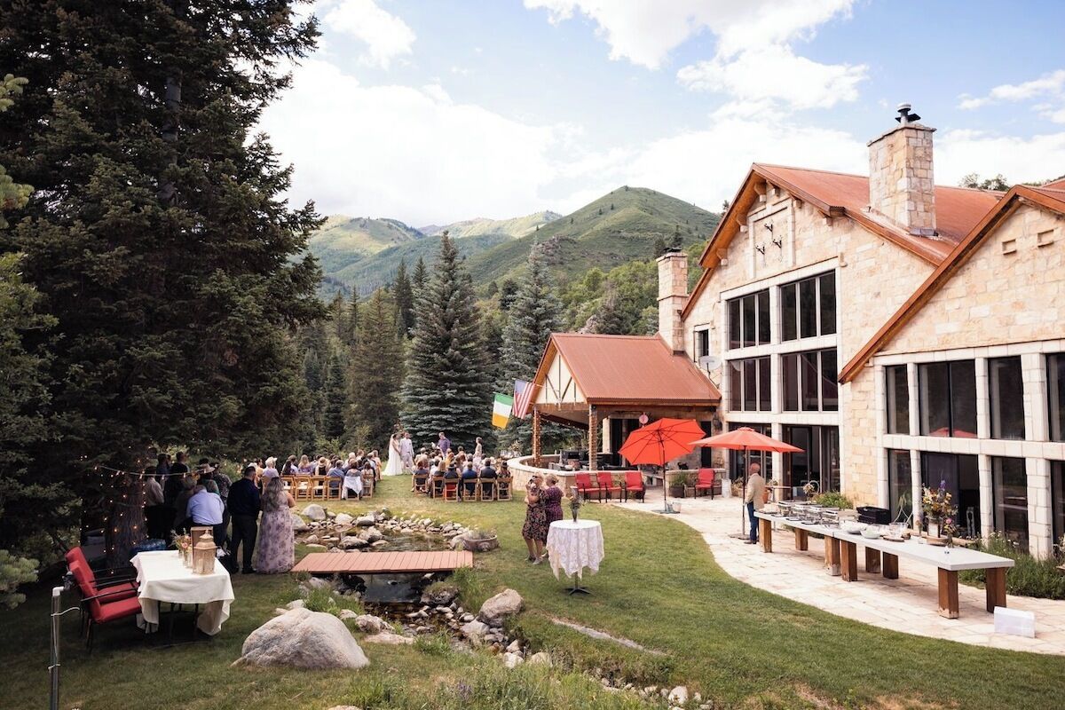 A lodge with stone architecture, outdoor dining, and a mountainous backdrop.