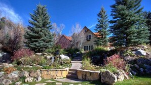 A house with a stone pathway leading to the entrance, surrounded by evergreen trees and a well-maintained garden. - Luxurious Mountain Retreat With Pool (Midway)