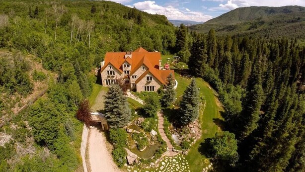 A large, two-story house with a red roof, surrounded by dense forest and hills. - Luxurious Mountain Retreat With Pool (Midway)