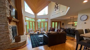 A spacious living room with a stone fireplace, wooden flooring, and large windows offering a view of the outdoors. - CR1 Bretton Woods (Bretton Woods)
