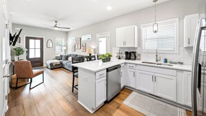 A modern kitchen with white cabinetry, a dishwasher, and a dining area with a gray sofa and a brown chair. - Whole Home 1012 & 1014 Franklin (Clarksville)