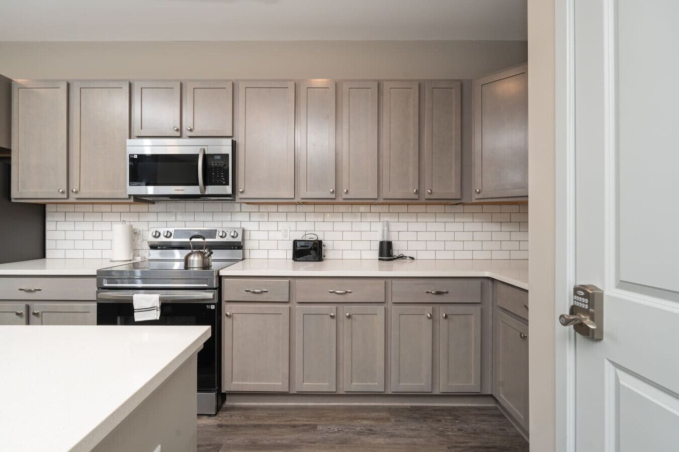 A modern kitchen with light wood cabinets, stainless steel appliances, and a white tiled backsplash.