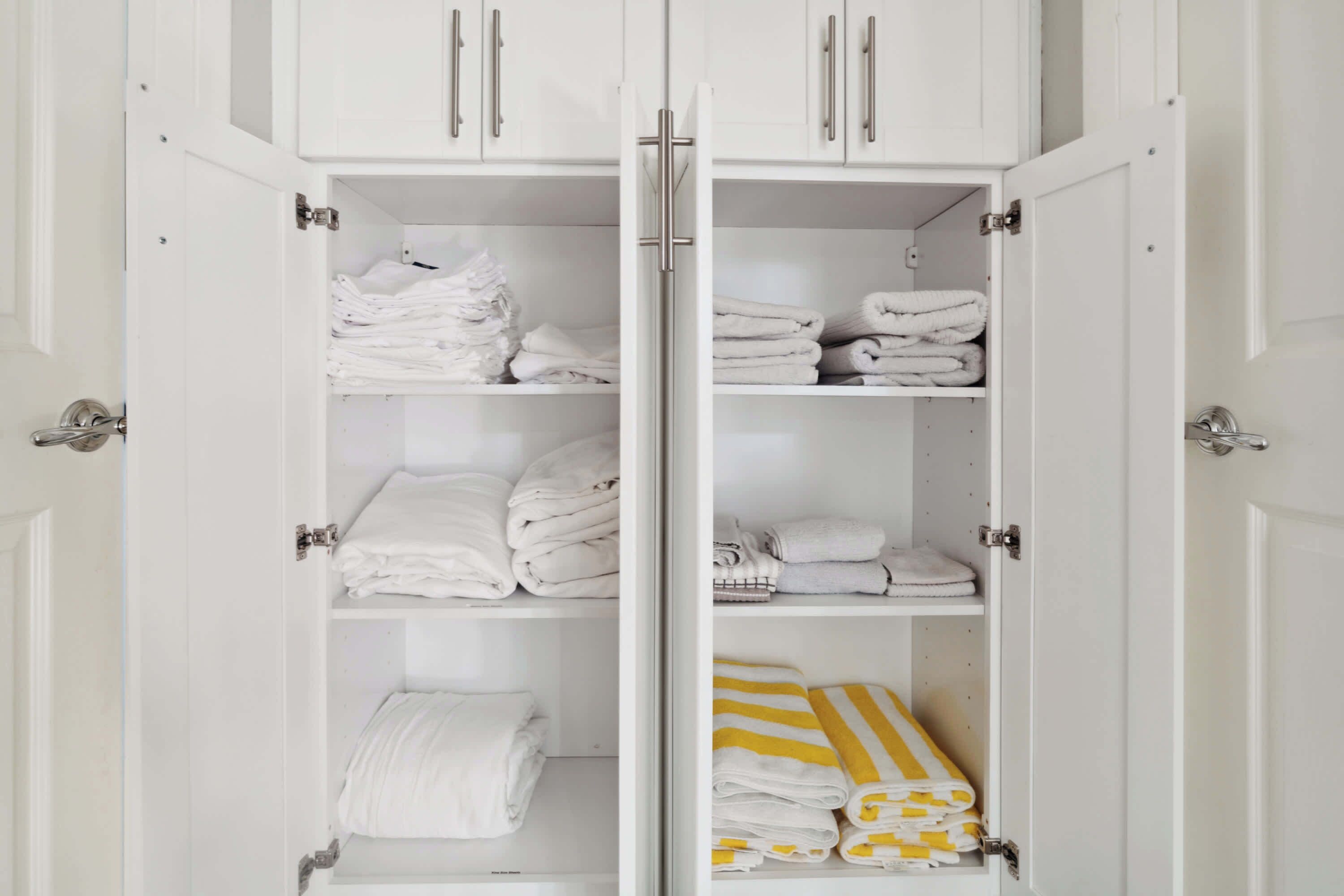 A white wardrobe with multiple shelves and doors, containing neatly folded white towels and a few striped towels.