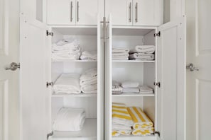 A white wardrobe with multiple shelves and doors, containing neatly folded white towels and a few striped towels. - Spacious Scottsdale Retreat With Pool (Tempe)