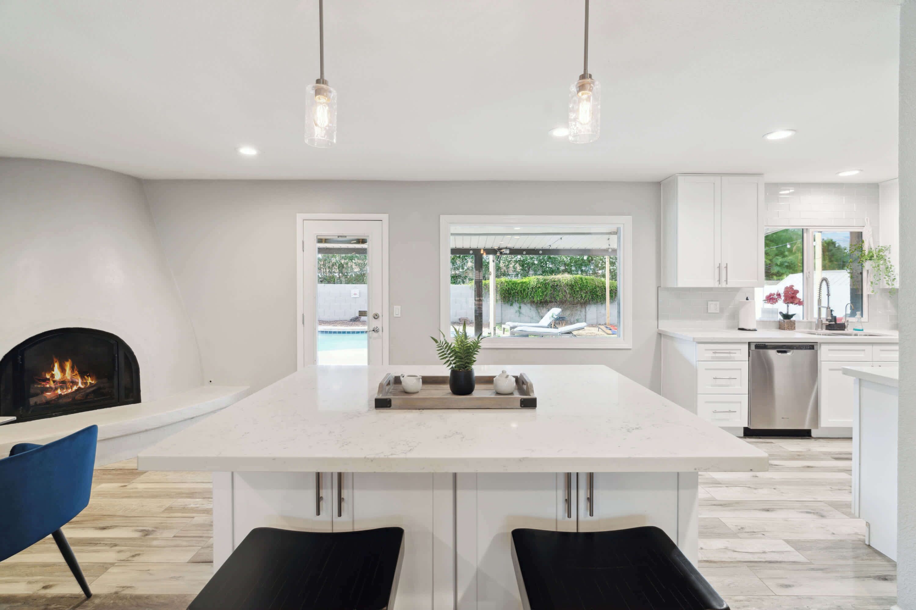 A modern kitchen with a central island, pendant lighting, a fireplace, and a view of the outdoors.