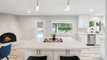 A modern kitchen with a central island, pendant lighting, a fireplace, and a view of the outdoors.