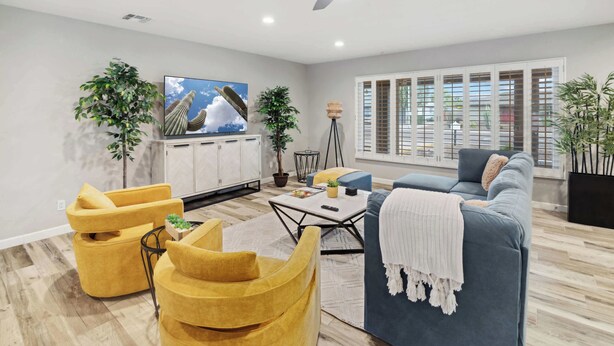 Un salon moderne avec un ventilateur de plafond, un téléviseur, un canapé et deux fauteuils jaunes.