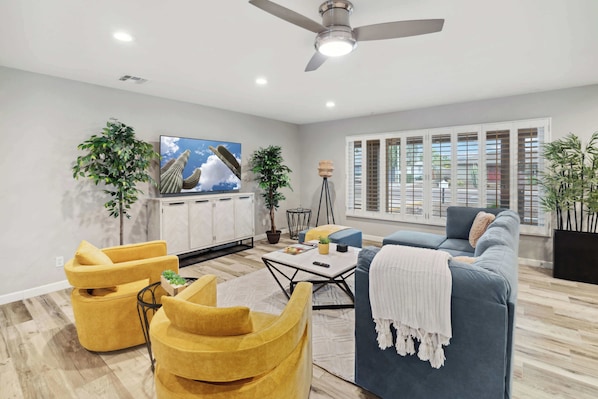 A modern living room with a ceiling fan, a TV, a sofa, and two yellow armchairs.