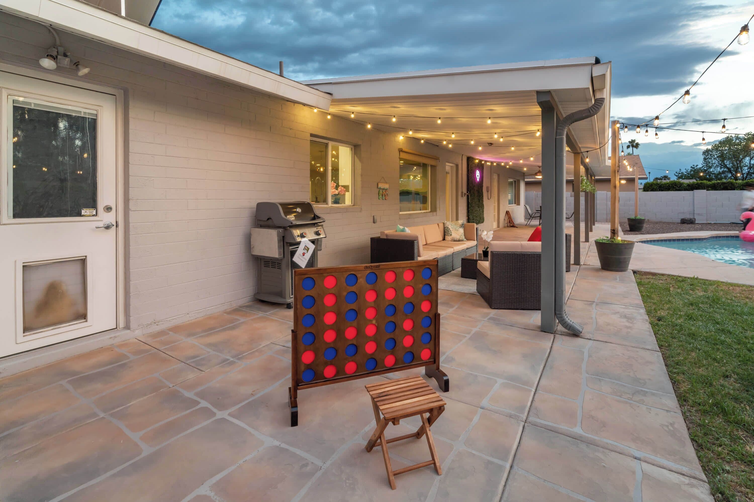 A patio with a pool, outdoor seating, string lights, and a grill.