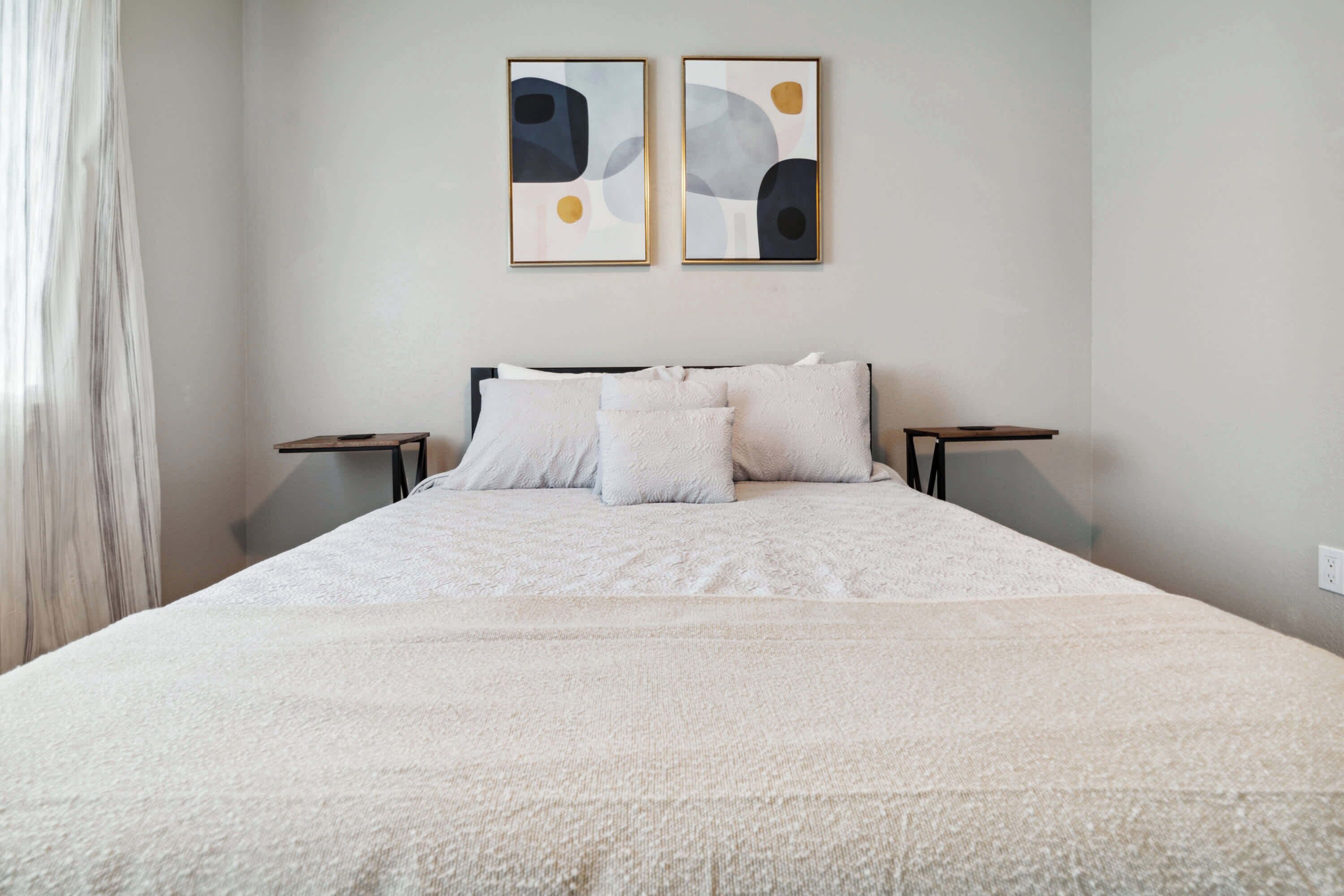 Een groot bed met een witte dekbedovertrek, twee nachtkastjes en abstracte wanddecoratie.