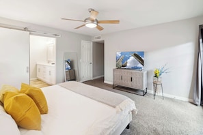 A bedroom with a bed, a ceiling fan, a dresser, a television, and a door leading to another room. - Spacious Scottsdale Retreat With Pool (Tempe)