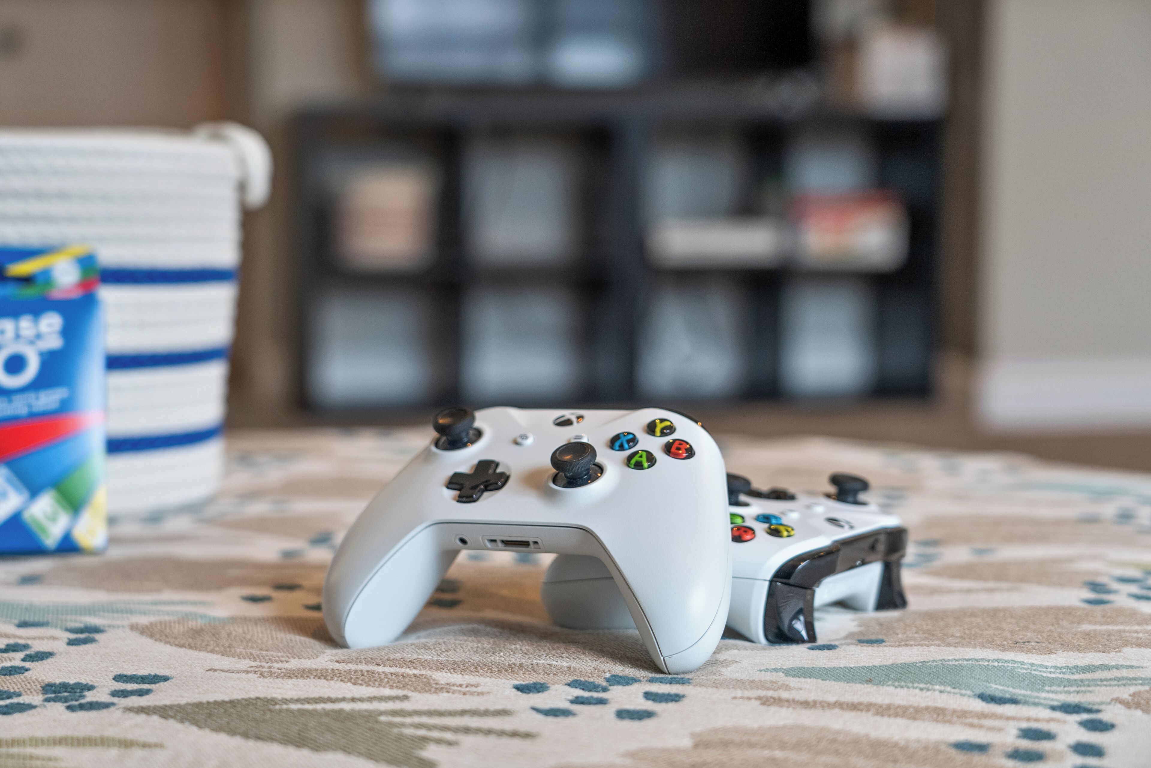 Une manette de jeu blanche, posée sur un tapis à motifs, avec un arrière-plan flou.
