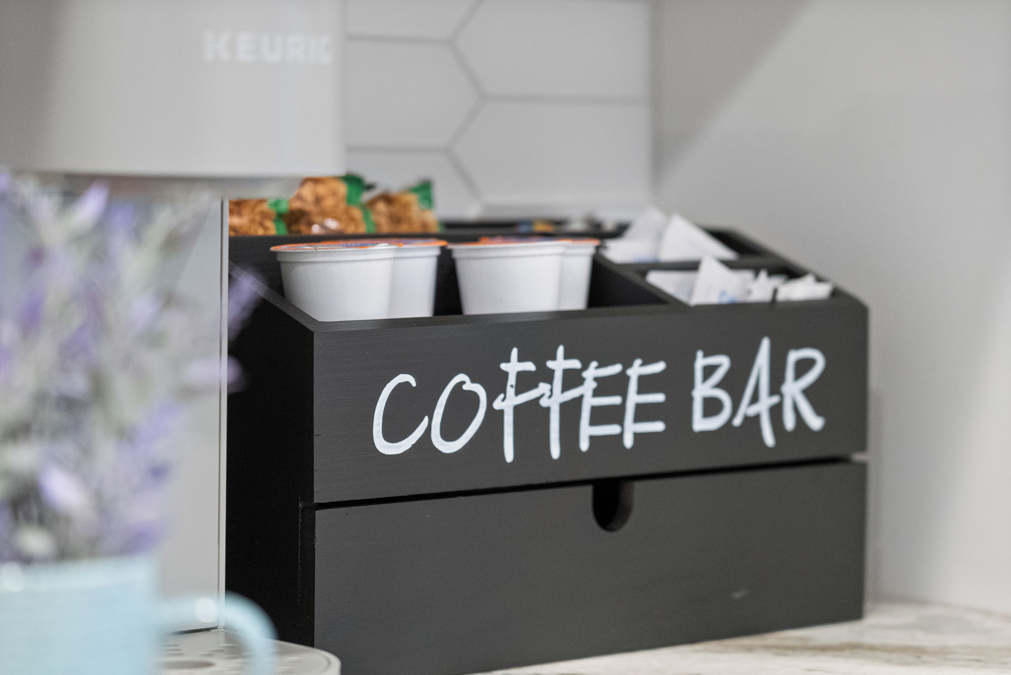A black storage box labeled 'COFFEE BAR' with several white cups and a green bag inside.