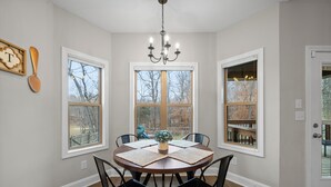 Une salle à manger avec une table ronde, quatre chaises, un lustre et de grandes fenêtres.