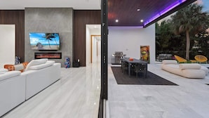 A modern living room with a flat-screen TV, a fireplace, and a dining area with outdoor seating. - Villa Pesara by Rove Travel Luxury Riverfront (Fort Lauderdale)