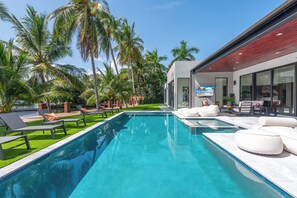 Ein moderner Poolbereich mit Liegestühlen, klarem Wasser und Palmen.