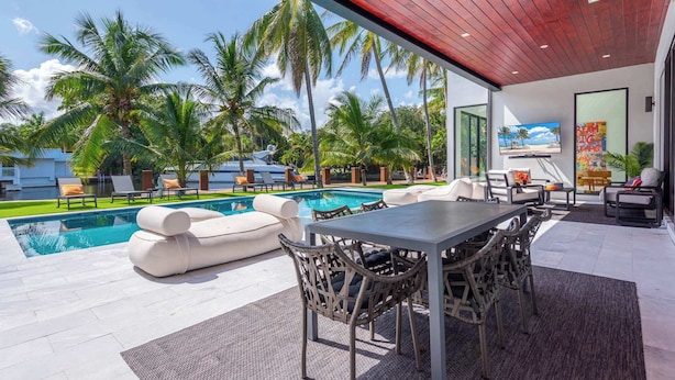An outdoor pool area with lounge chairs, a dining table, and a TV screen. - Villa Pesara by Rove Travel Luxury Riverfront (Fort Lauderdale)