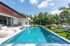 Ein modernes Haus mit Swimmingpool, Gartenmöbeln und einem gepflegten Rasen.