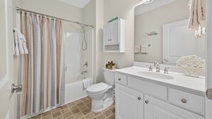 Ein Badezimmer mit Duschvorhang, Toilette, Waschbecken, Schrank und Spiegel.