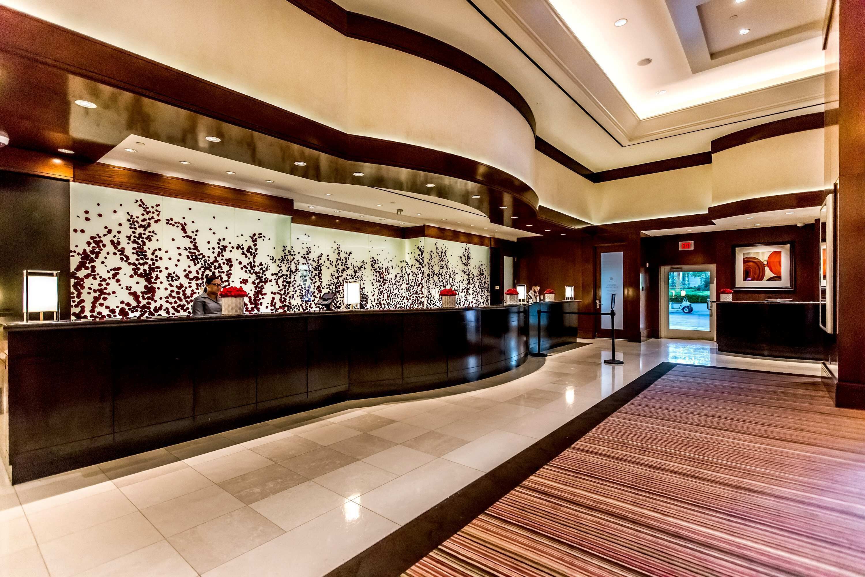 A modern hotel lobby with a curved reception desk, a large abstract wall art, and a clean, tiled floor.