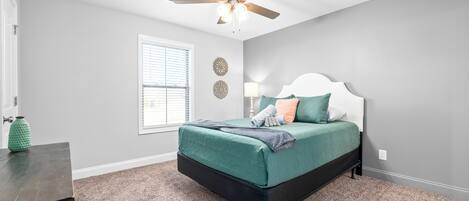 A bedroom with a bed, a ceiling fan, a window, and a nightstand.