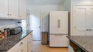 A kitchen with white cabinets, a granite countertop, a toaster, a blender, and a trash can. - Driftwood Cottage by Rovetravel 3BR Quiet Cottage (East Hampton)
