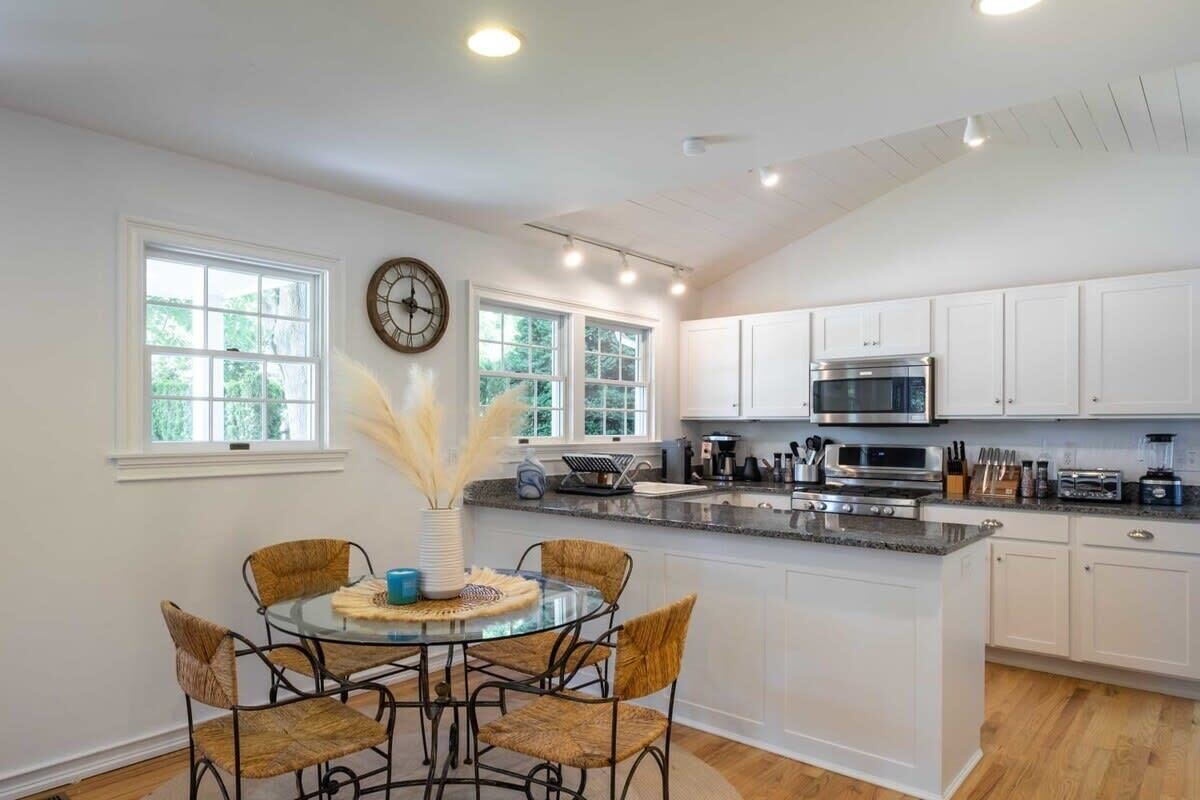 A kitchen with white cabinets, a central island, and a dining area with wicker chairs.