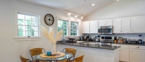 A kitchen with white cabinets, a central island, and a dining area with wicker chairs.