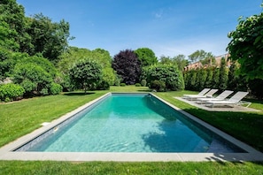 Una piscina rectangular con superficie de agua azul cristalina, rodeada de césped bien cuidado y varios árboles.