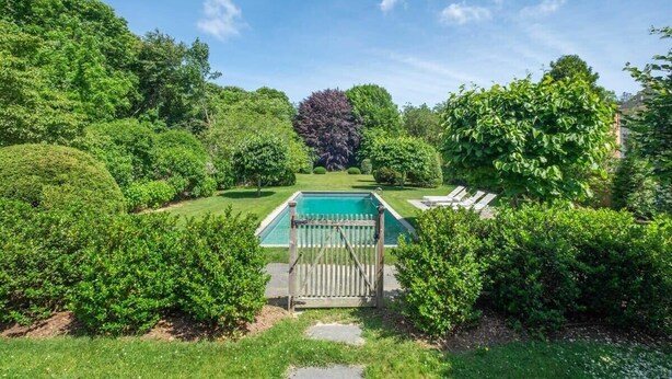 A swimming pool surrounded by lush greenery and a wooden fence. - Driftwood Cottage by Rovetravel 3BR Quiet Cottage (East Hampton)