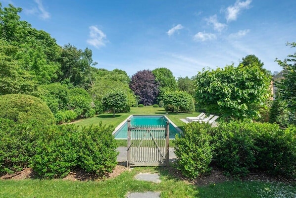 Una piscina rodeada de abundante vegetación y una cerca de madera.