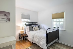 A bedroom with a bed, bedside table, lamp, and two windows. - Driftwood Cottage by Rovetravel 3BR Quiet Cottage (East Hampton)