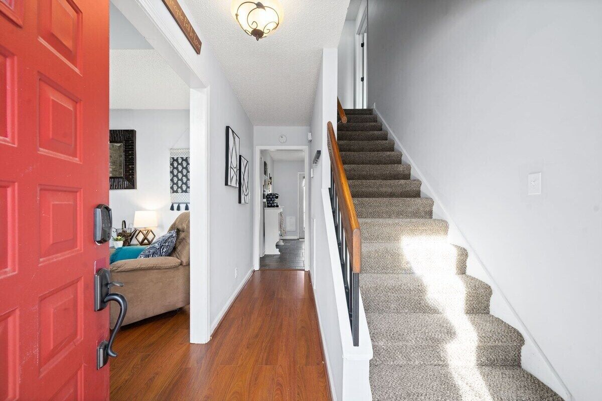 Un pasillo con una puerta roja, una escalera con peldaños alfombrados y un pasamanos de madera.