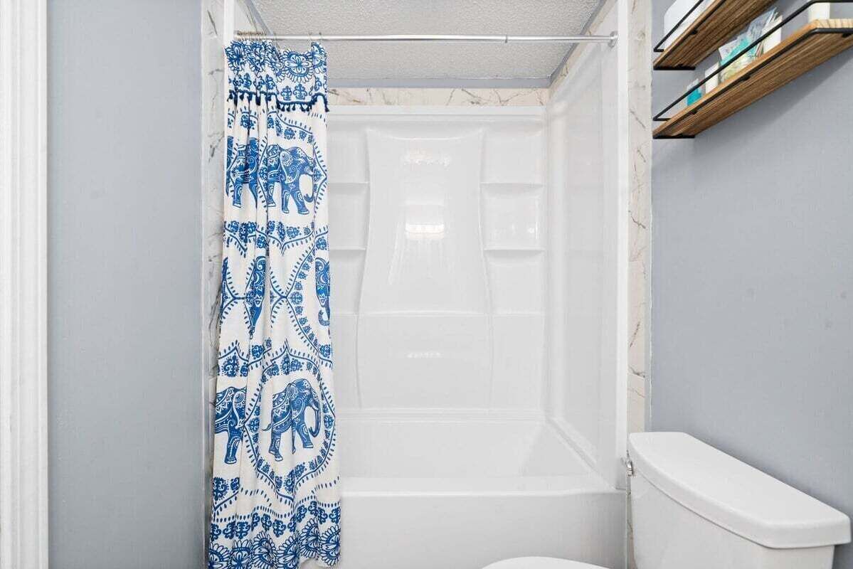 Un baño con ducha, inodoro y un estante con libros.
