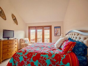 A bedroom with a bed, a dresser, a television, and a window with a view.