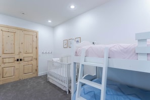 Una habitación infantil con una cama litera, una cuna, un armario y una estantería de pared.